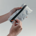 Close up of hands holding the Off-White packable Ultra Light Crossbody Bag packed into it's pocket